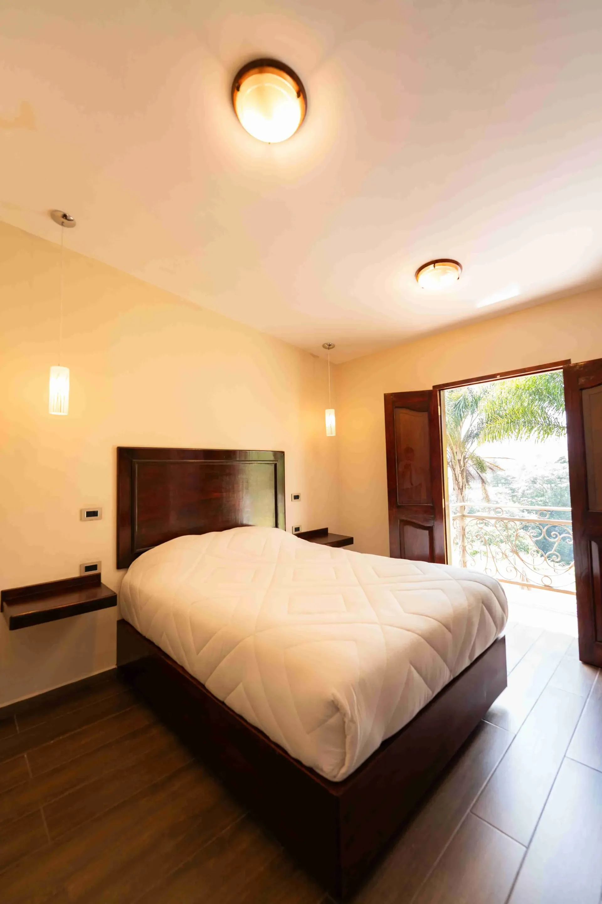 Bright bedroom with a large bed, tiled floor, and open doors to a sunny outdoor view.