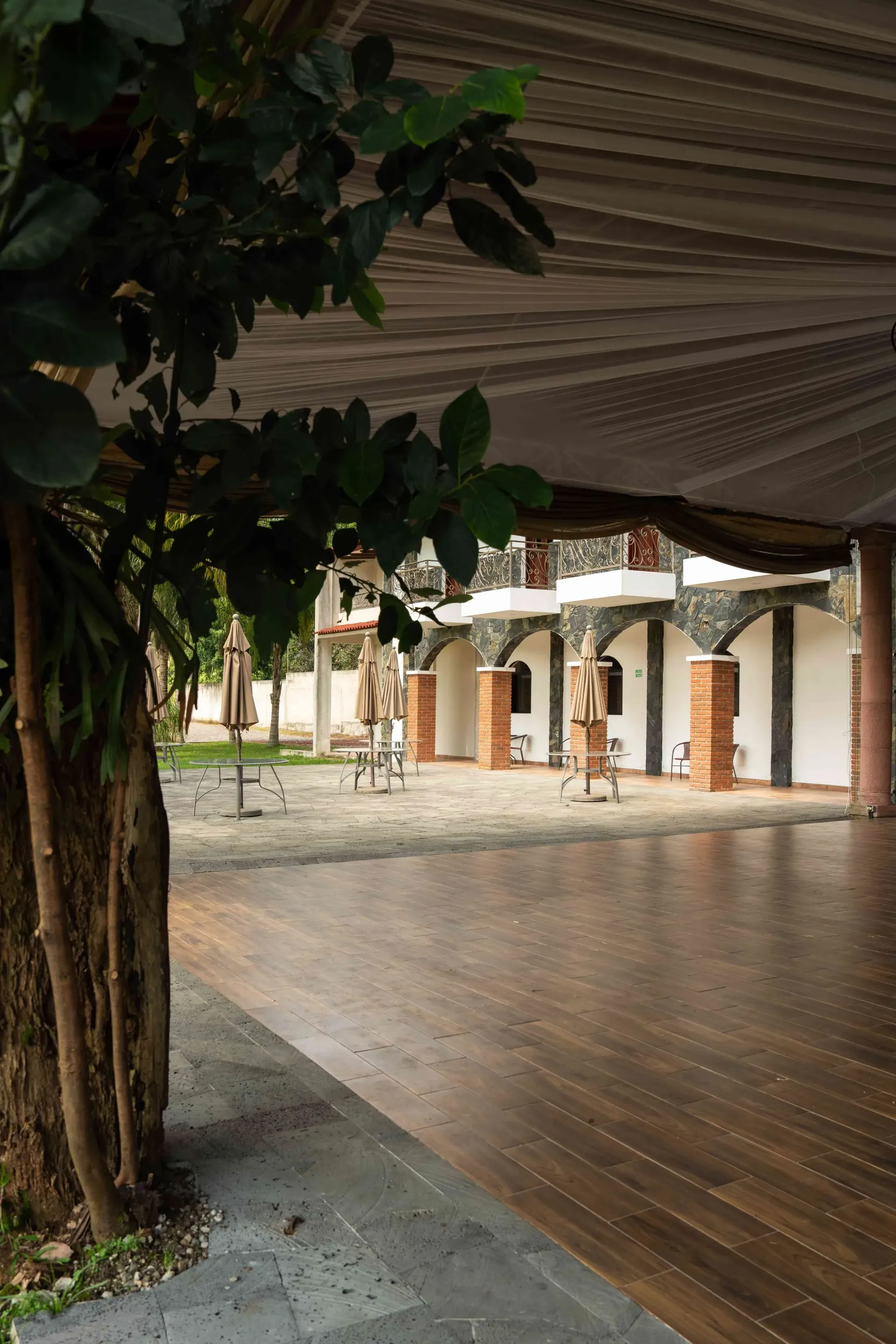 Rainy covered courtyard with wooden floor, stone columns, and trees framing the scene