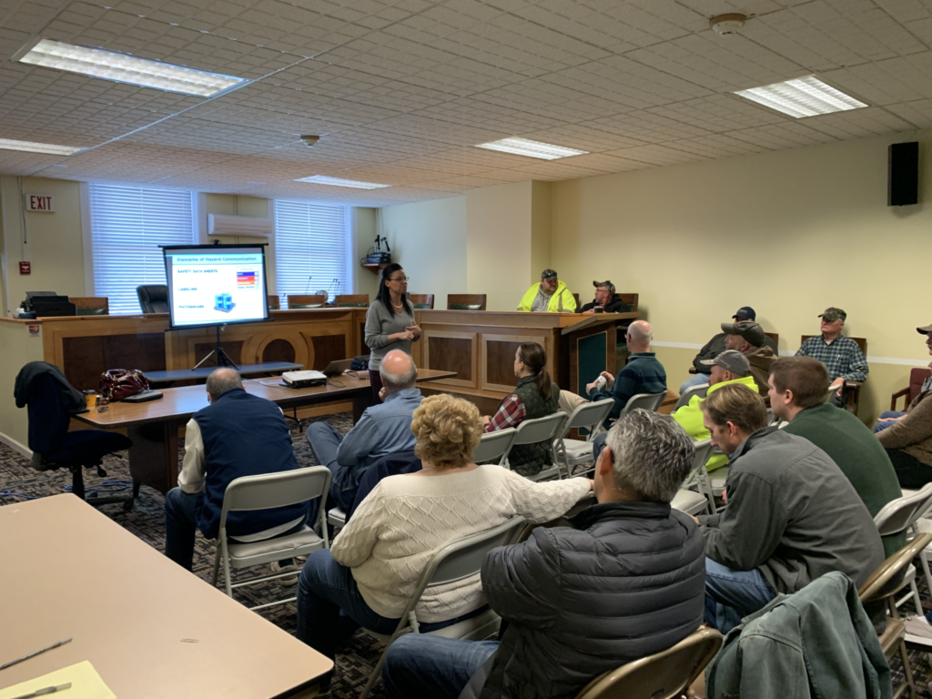 Community meeting in a conference room, with people seated and a presentation projected at the front.