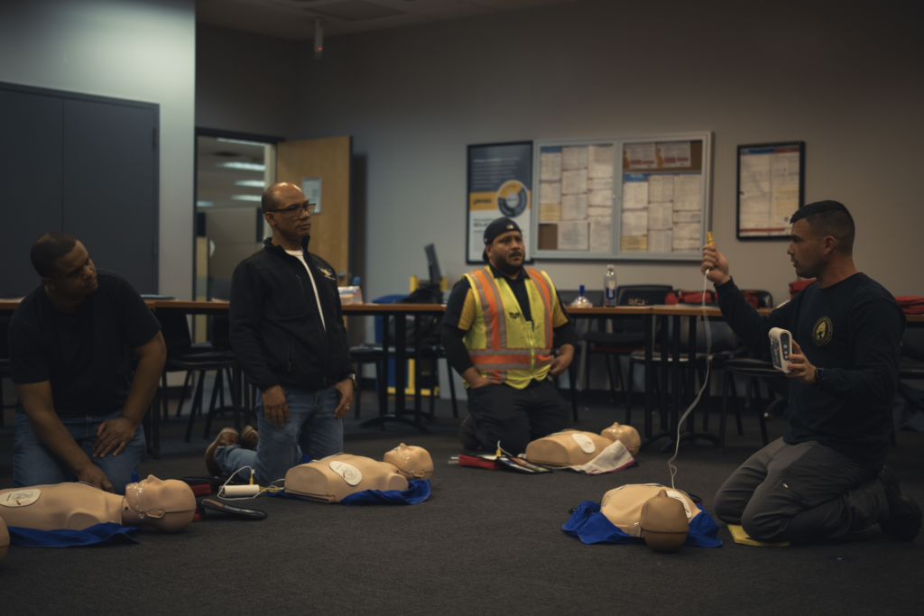 People kneeling in a training room beside mannequin torsos, practicing emergency response.