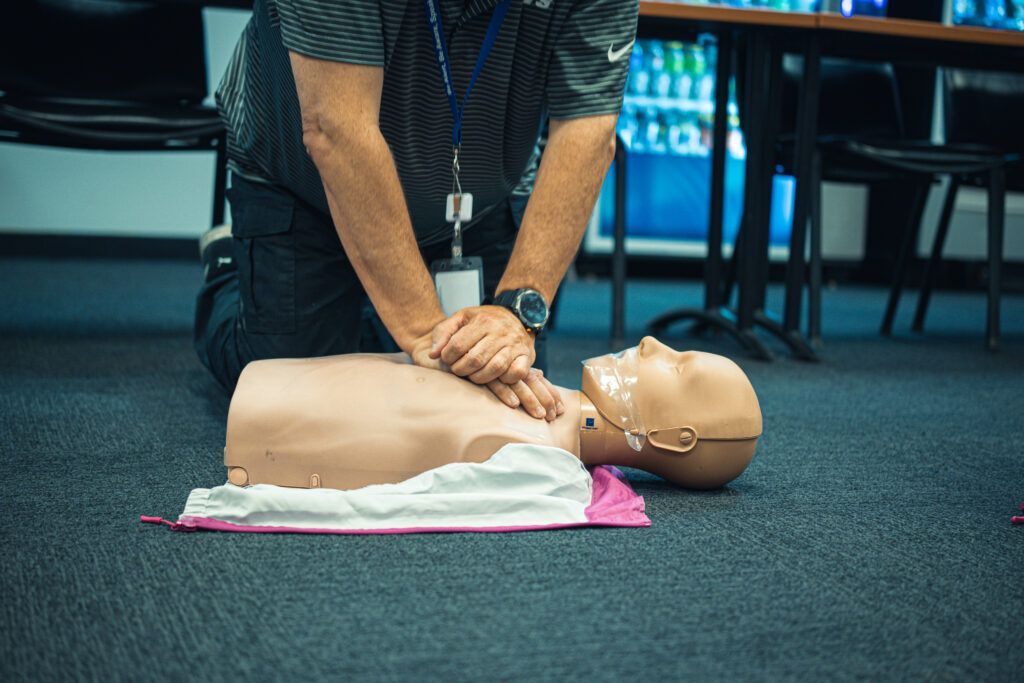 Person practicing CPR on a training manikin on the floor in a classroom setting