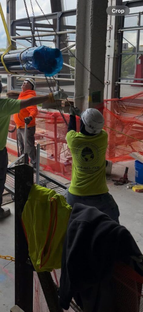 Worker in neon vest lifting blue material behind orange safety netting at a construction site