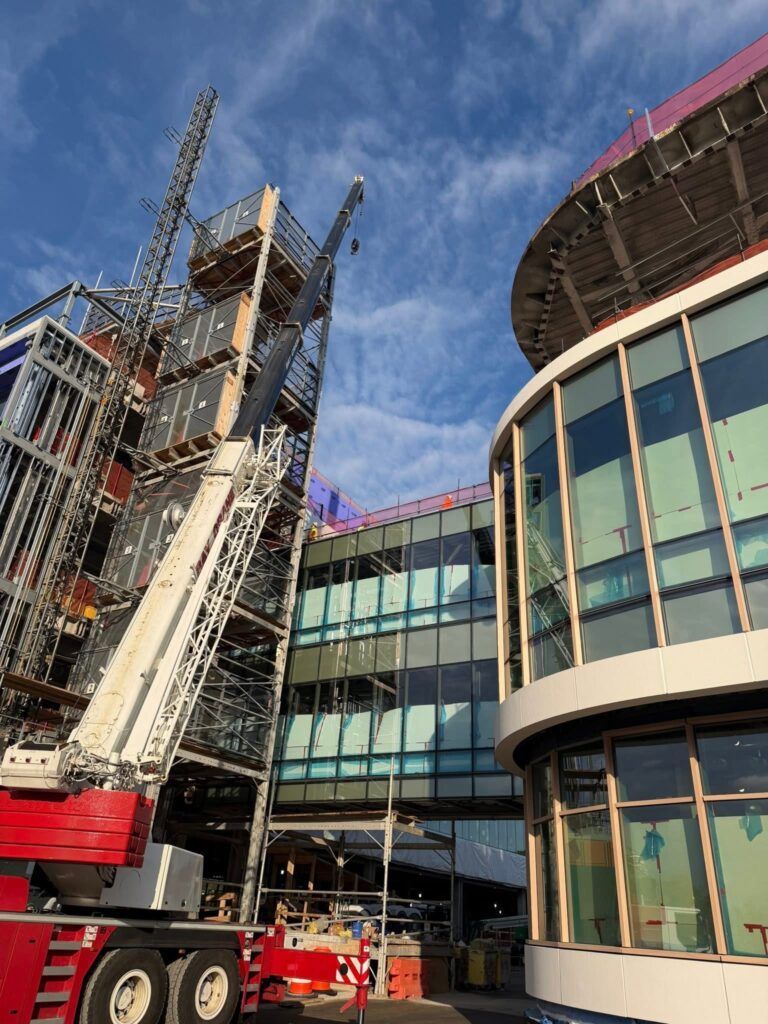 Construction site with crane beside a modern glass building under a blue sky