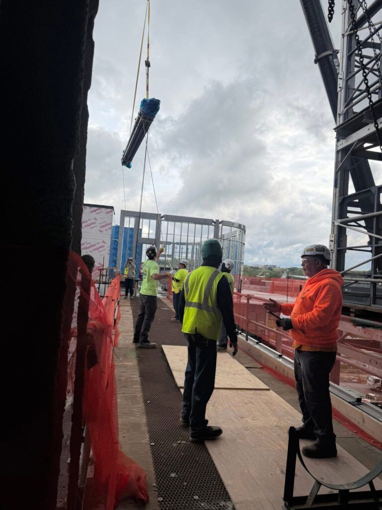 Workers in high-visibility gear guide a suspended load at a construction site.