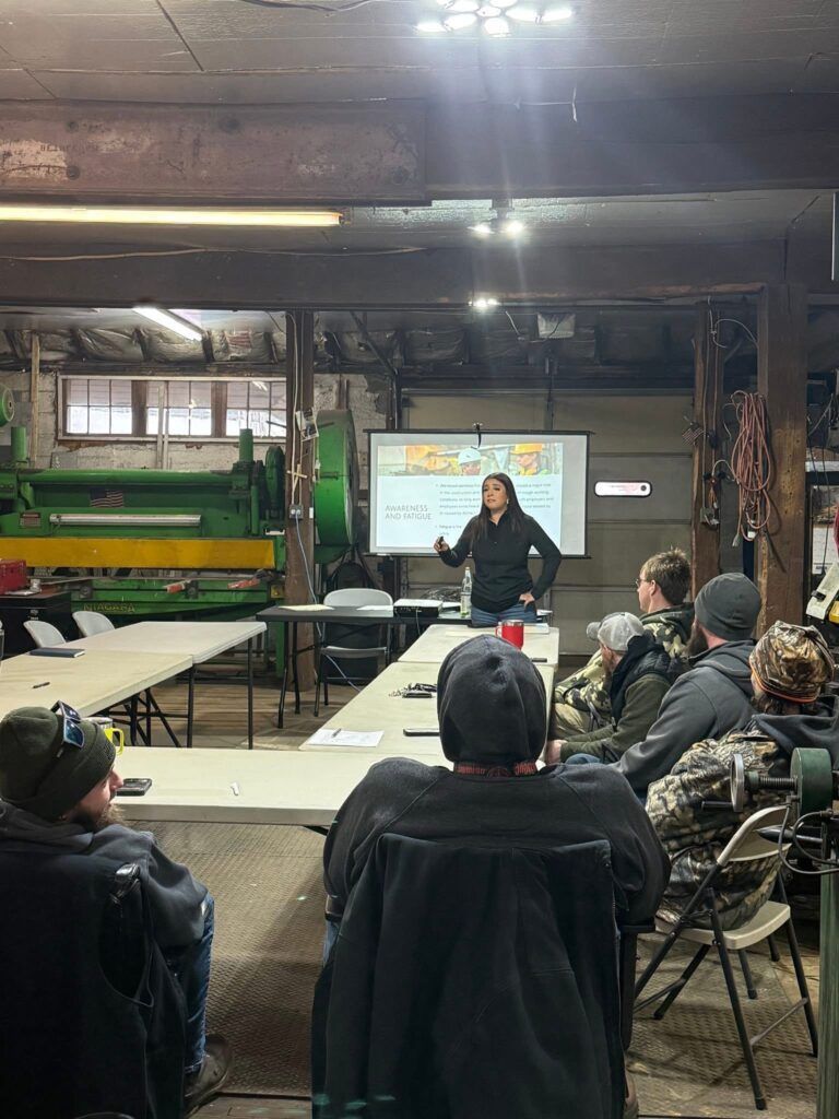 People seated in a workshop room watching a presenter beside a projected slide.