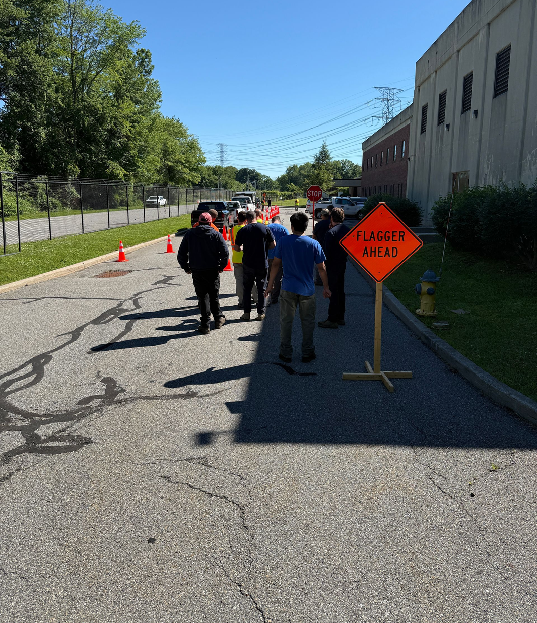 People walking on a gravel path beside a building with orange construction signs and cones.