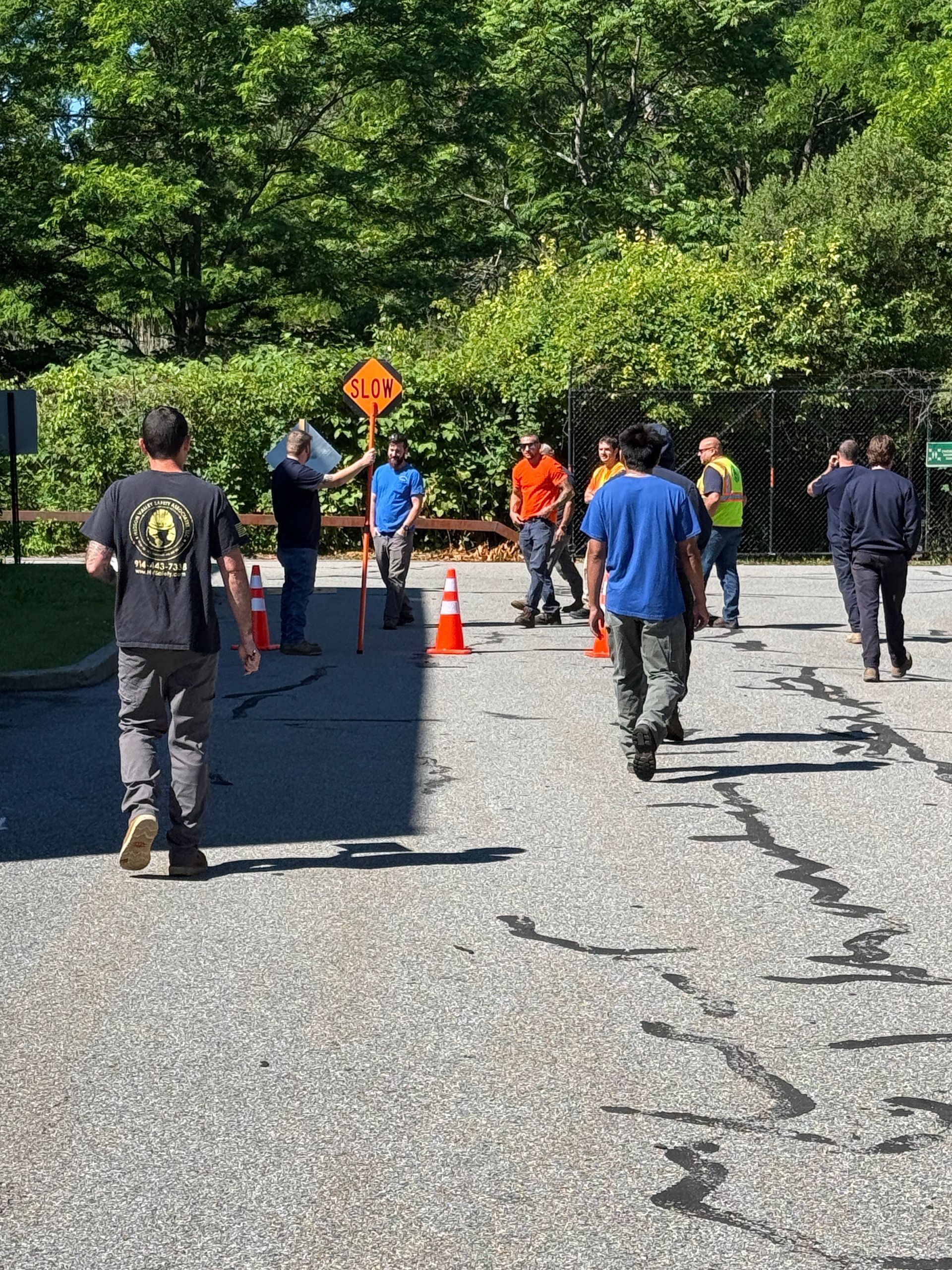 Workers in neon vests set orange cones outside a white building with an arched entrance.