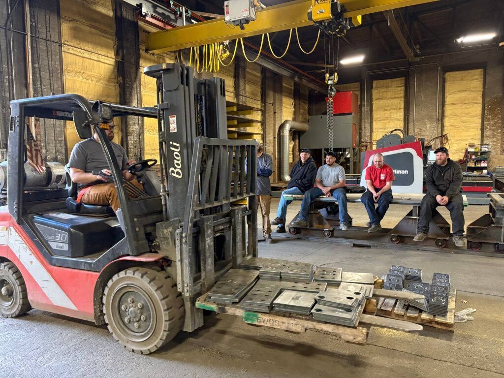 Forklift moving pallets in a warehouse, with people watching nearby.