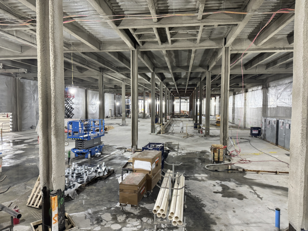 Empty industrial warehouse under construction with concrete pillars, scaffolding, tools, and stacked materials
