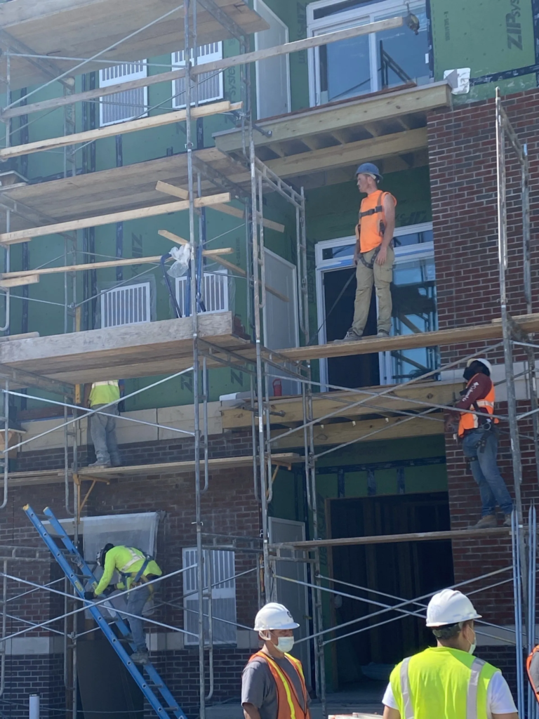 Construction workers on scaffolding outside a building, wearing hard hats and safety vests.