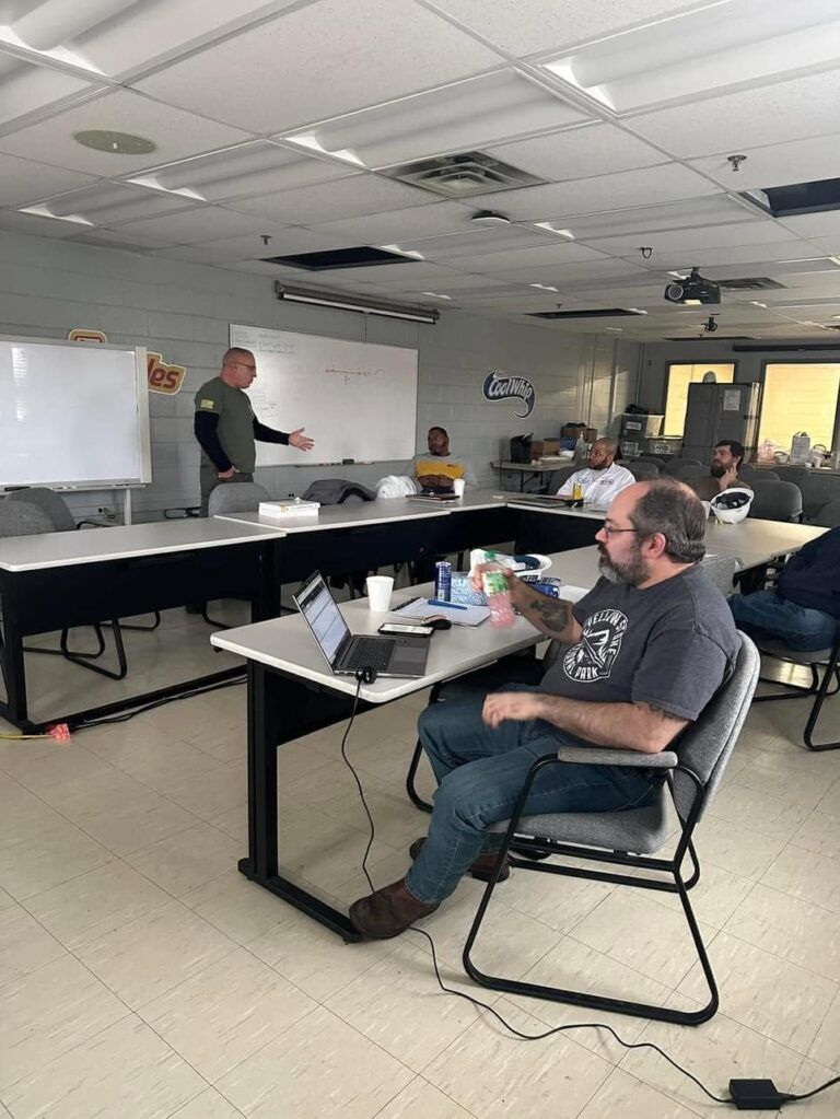 Office meeting with people seated at tables while a presenter writes on a whiteboard