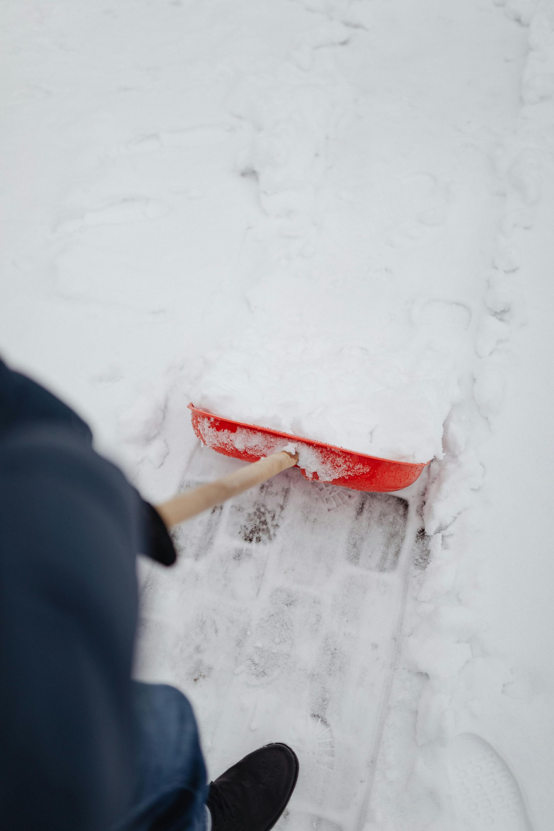 Person shoveling snow with a red snow shovel on a snowy sidewalk