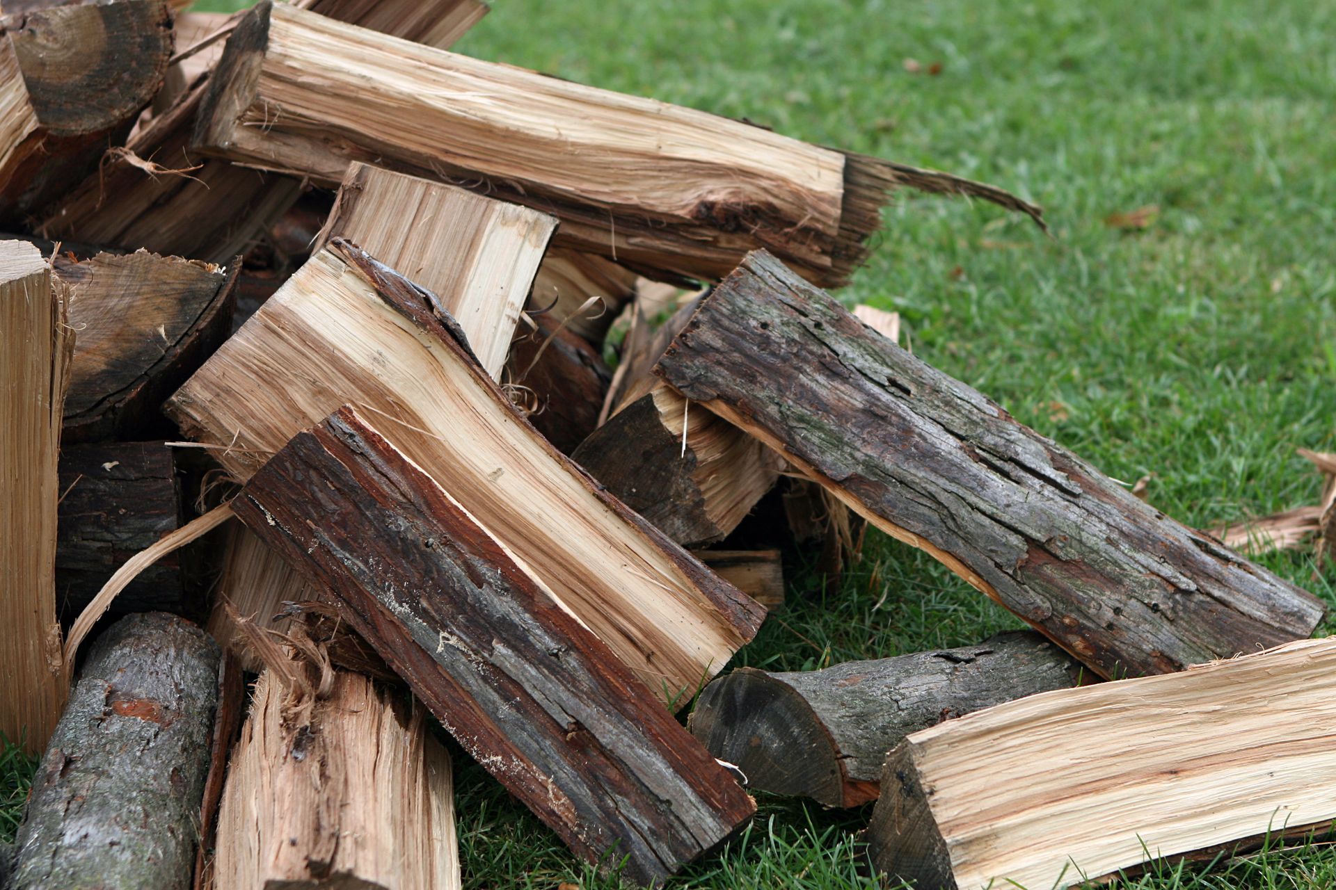Stack of split firewood on grass, with brown bark and pale wood grain visible