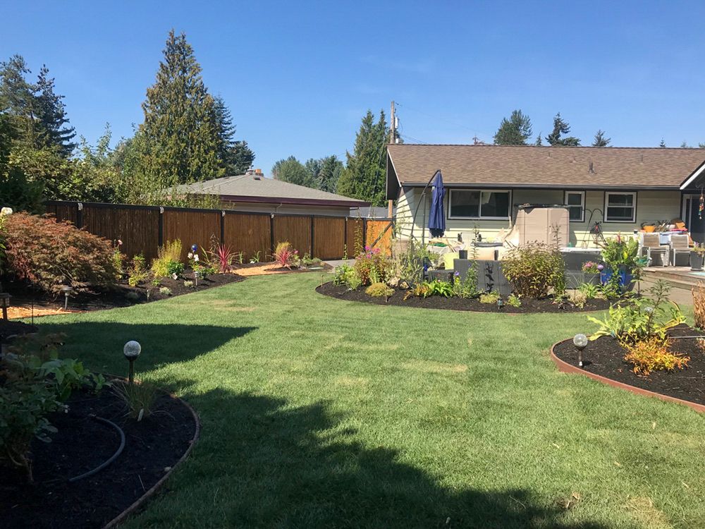 Spacious backyard with green lawn, mulched flower beds, and various plants.
