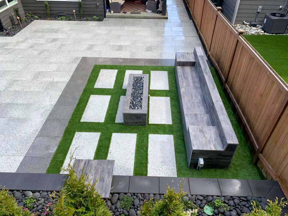 Backyard patio with a green-and-white paved section, raised planter, and wooden fence seating area.