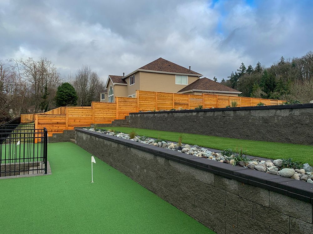 Terraced backyard with artificial putting green, stone walls, and wooden fence.