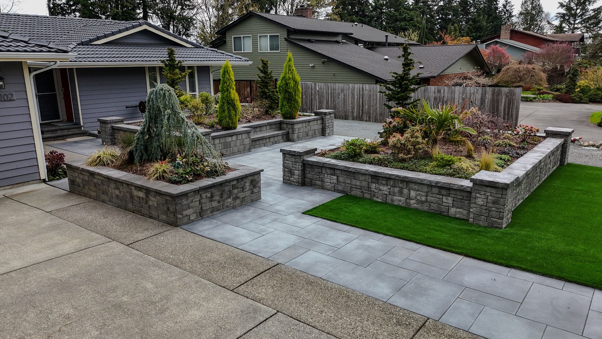 Gray concrete front yard with raised garden beds and evergreen landscaping.