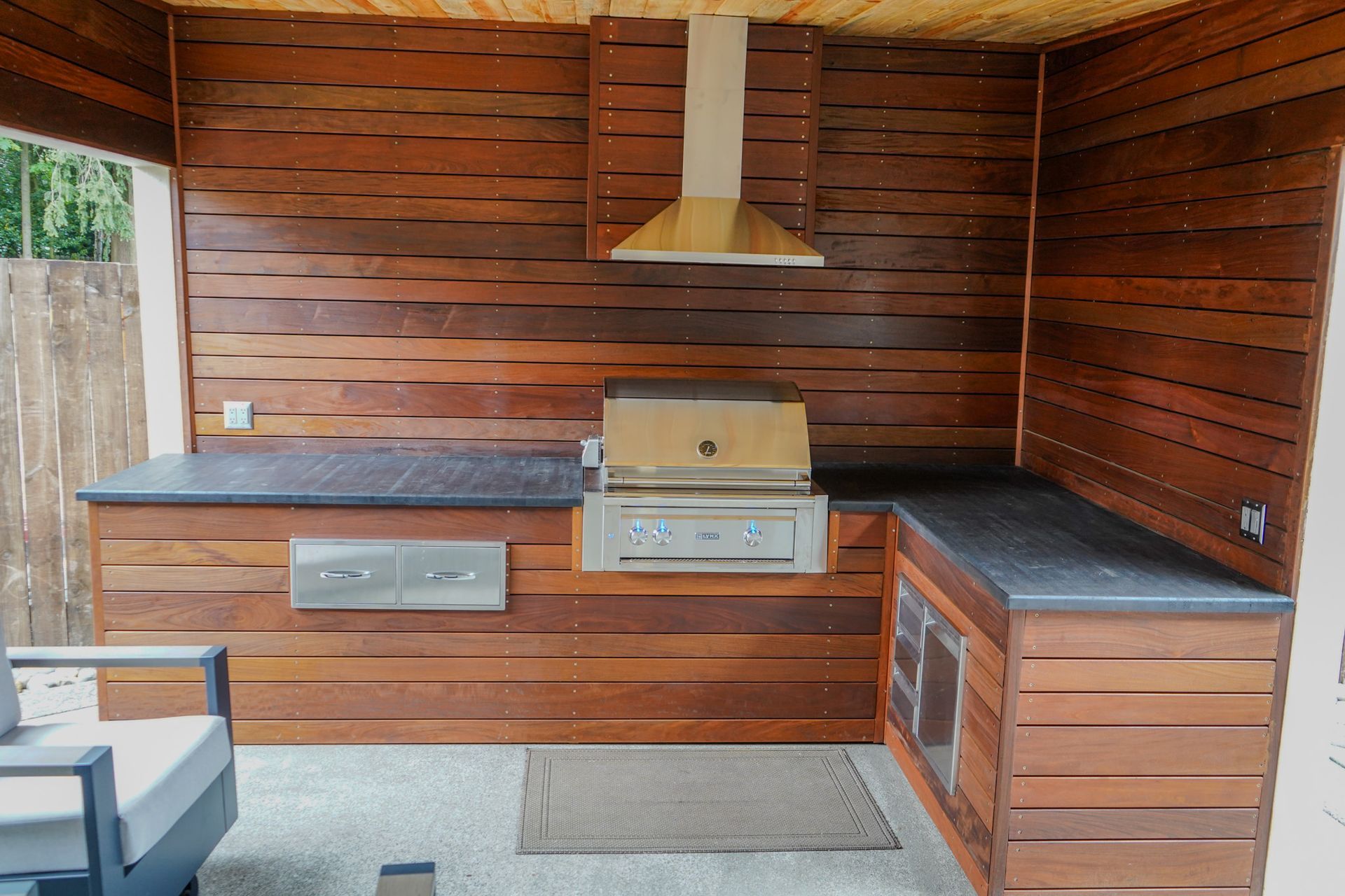 Outdoor kitchen with wood paneling, stainless steel grill, and granite countertops.