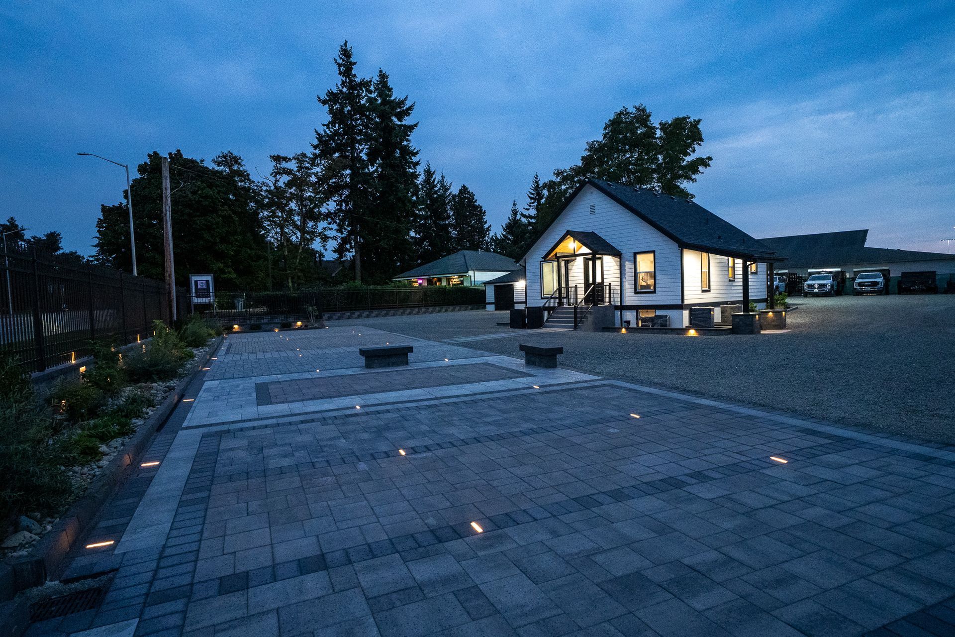 Night shot of a small white building with a lit-up entrance and paved parking area.