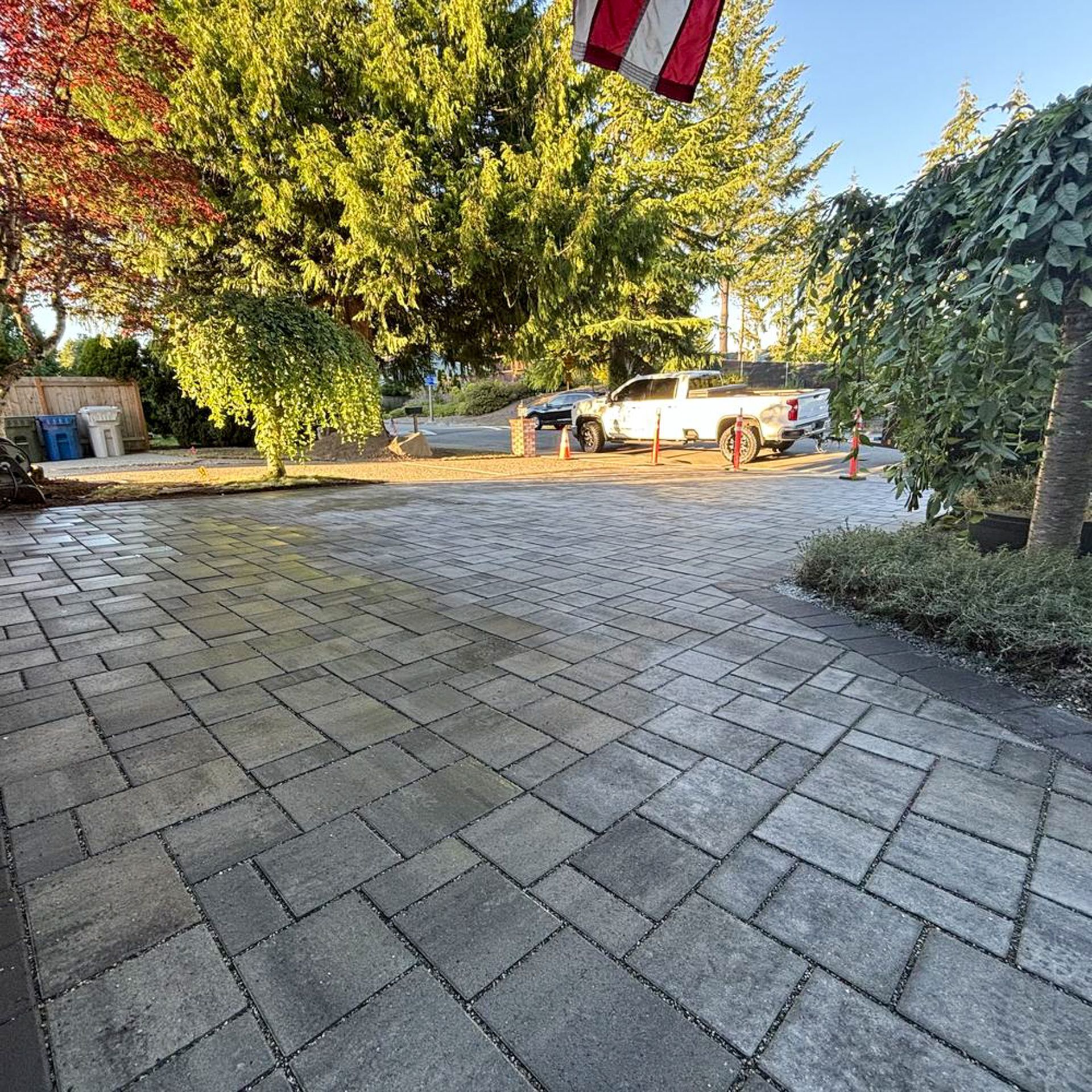 Brick driveway with a white truck parked, trees, and a flag in the background.
