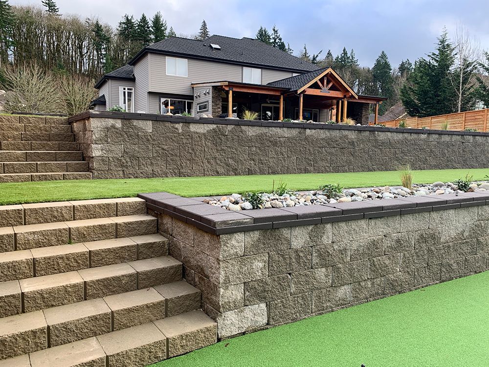 A multi-tiered landscaped yard with retaining walls and steps leading to a house with a covered patio.