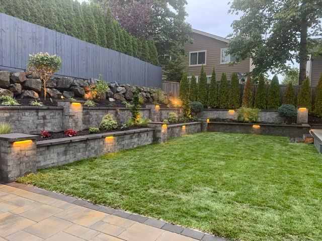 A tiered backyard with stone retaining walls, lush green grass, and built-in lights.