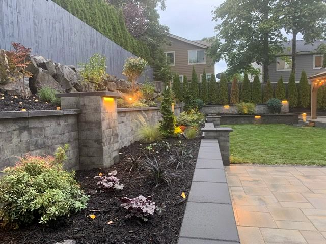 Stone retaining walls and landscaped garden with lighting in backyard setting.