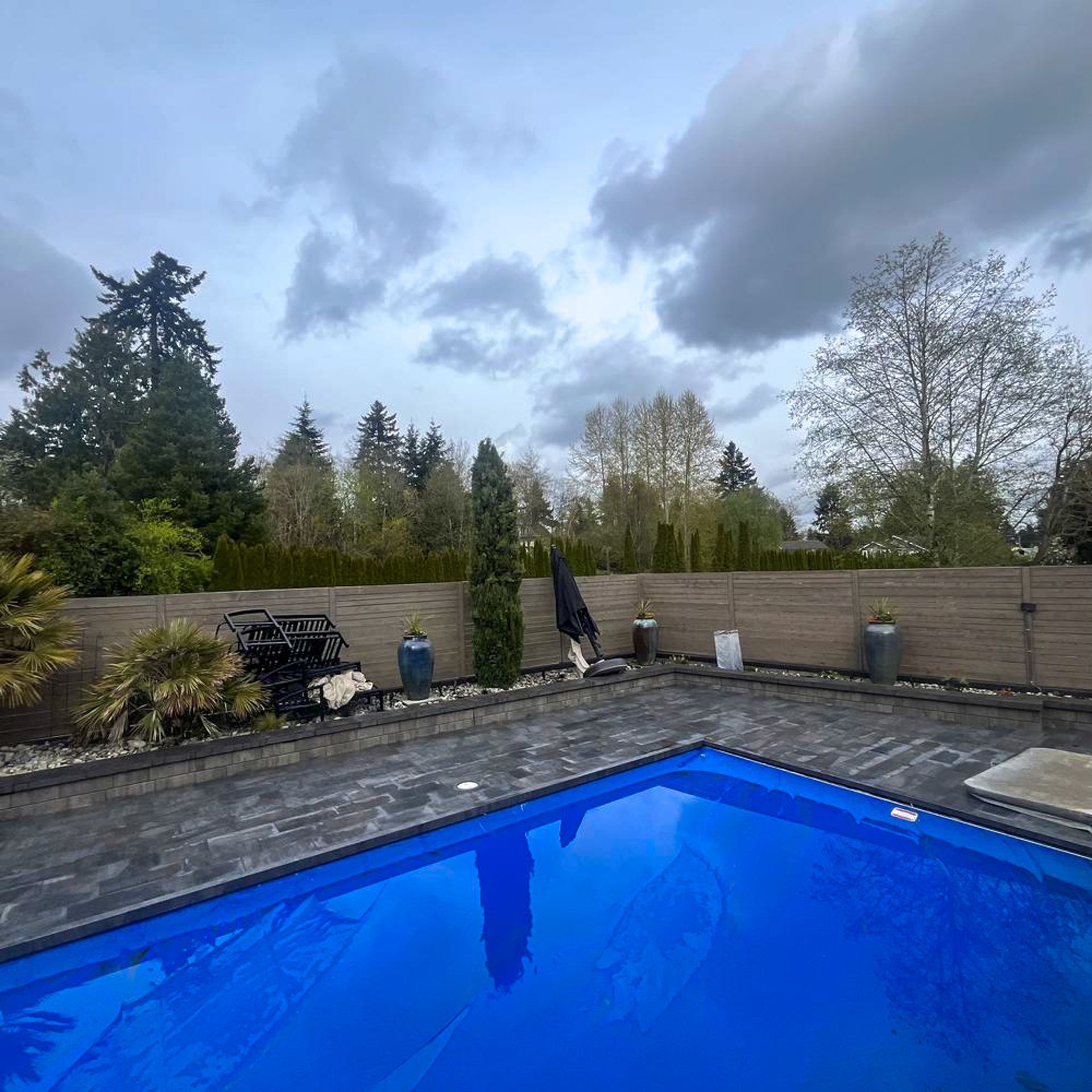 Backyard with pool, covered in blue, trees and cloudy sky.
