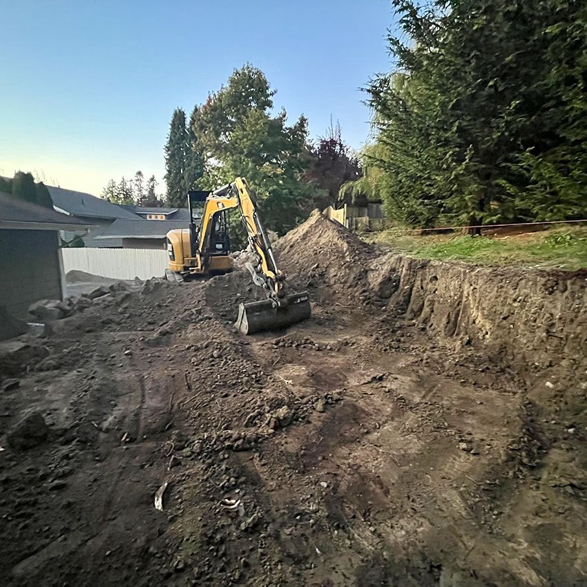Excavator digging a hole in a yard, dirt piles, trees and houses in background.
