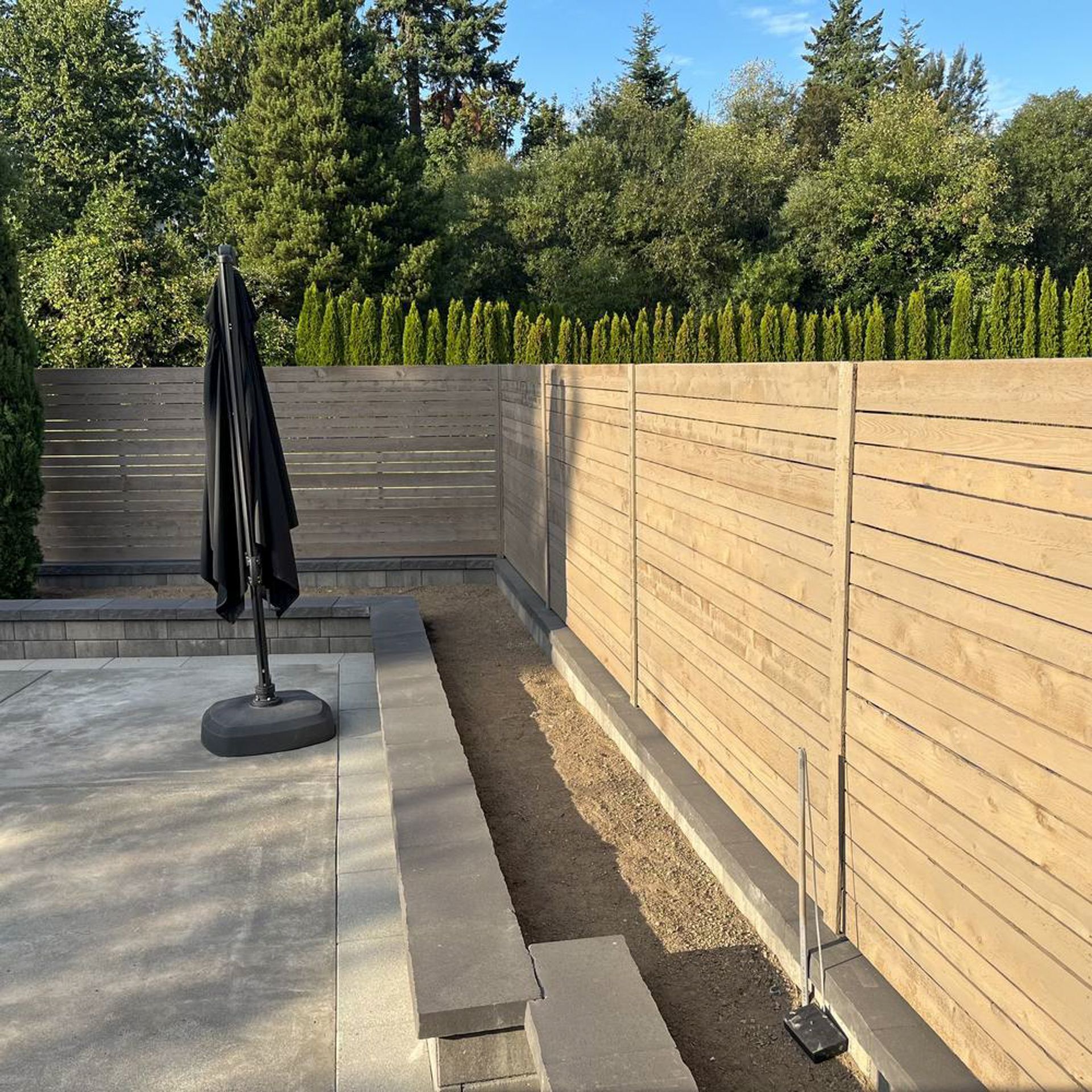 Backyard with wooden fence, concrete patio, and a black umbrella.