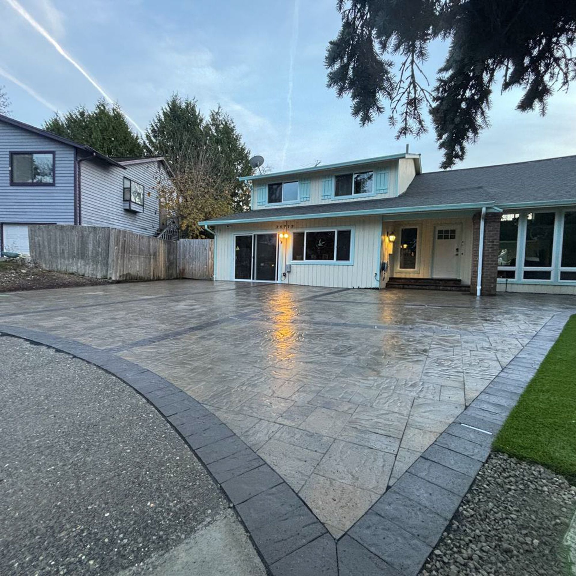 Driveway in front of a two-story house with stamped concrete and a dark brick border.