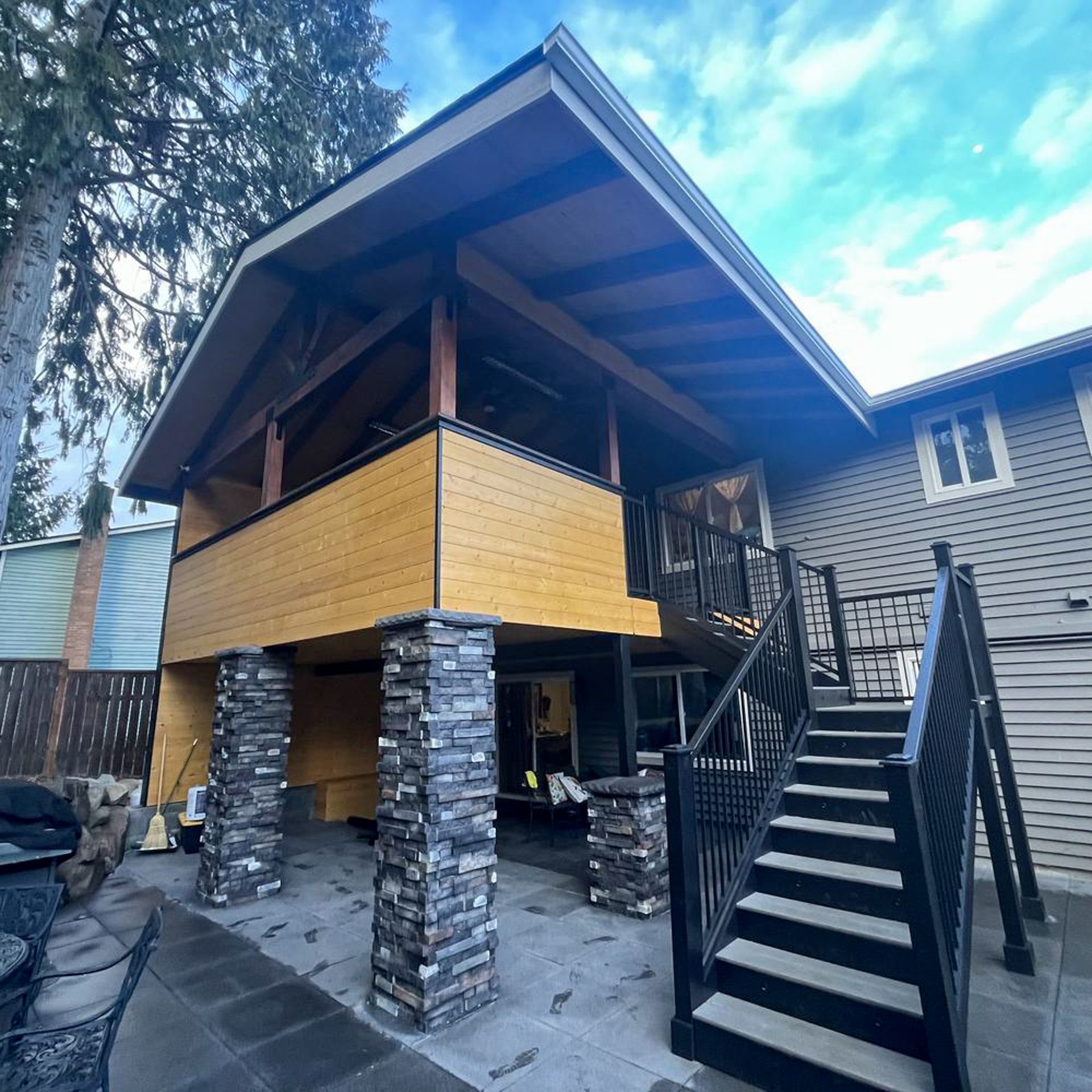 Covered patio addition on a house with stone pillars and black stairs.