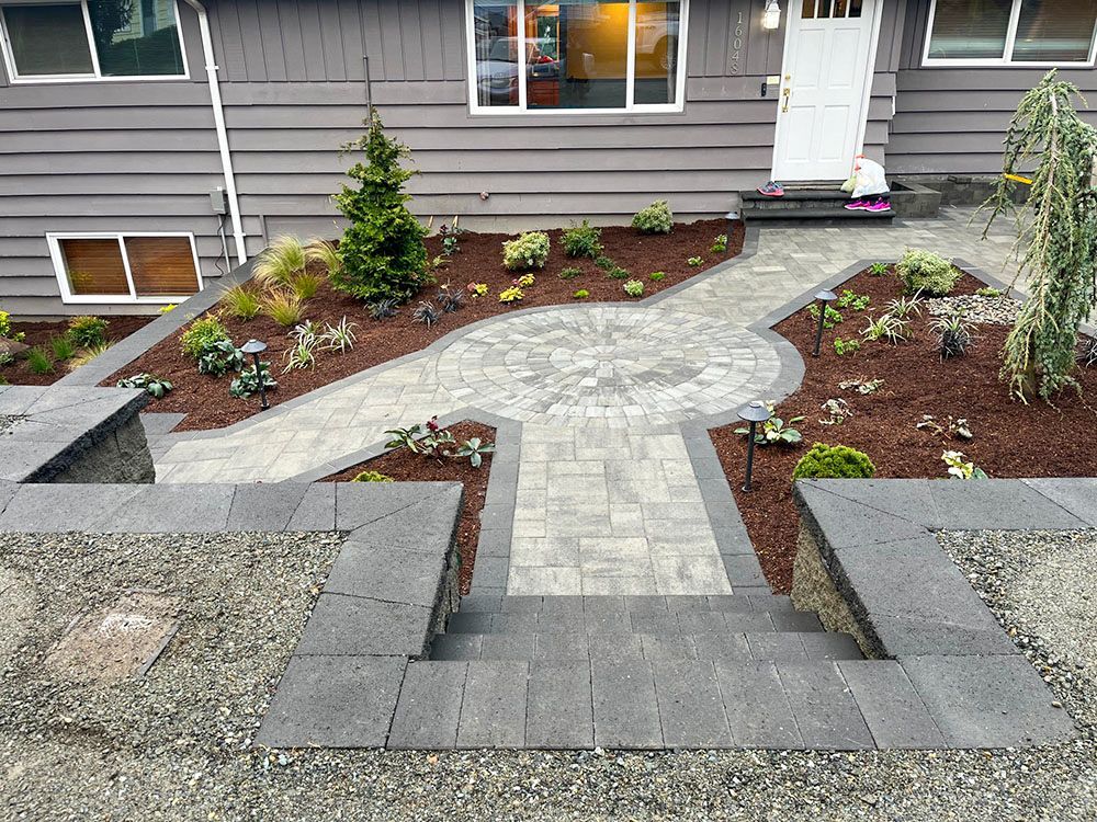 Gray stone steps and pathway lead to a front door, landscaping beds with plants on either side.