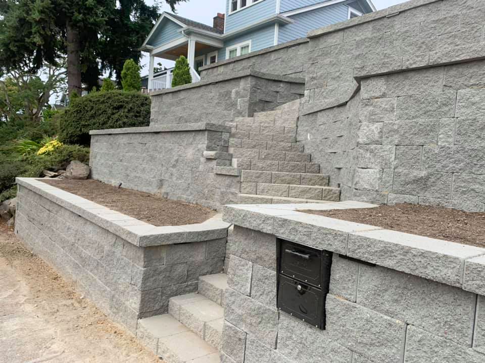 Stone retaining walls with steps leading up to a light blue house. Black mailbox visible.