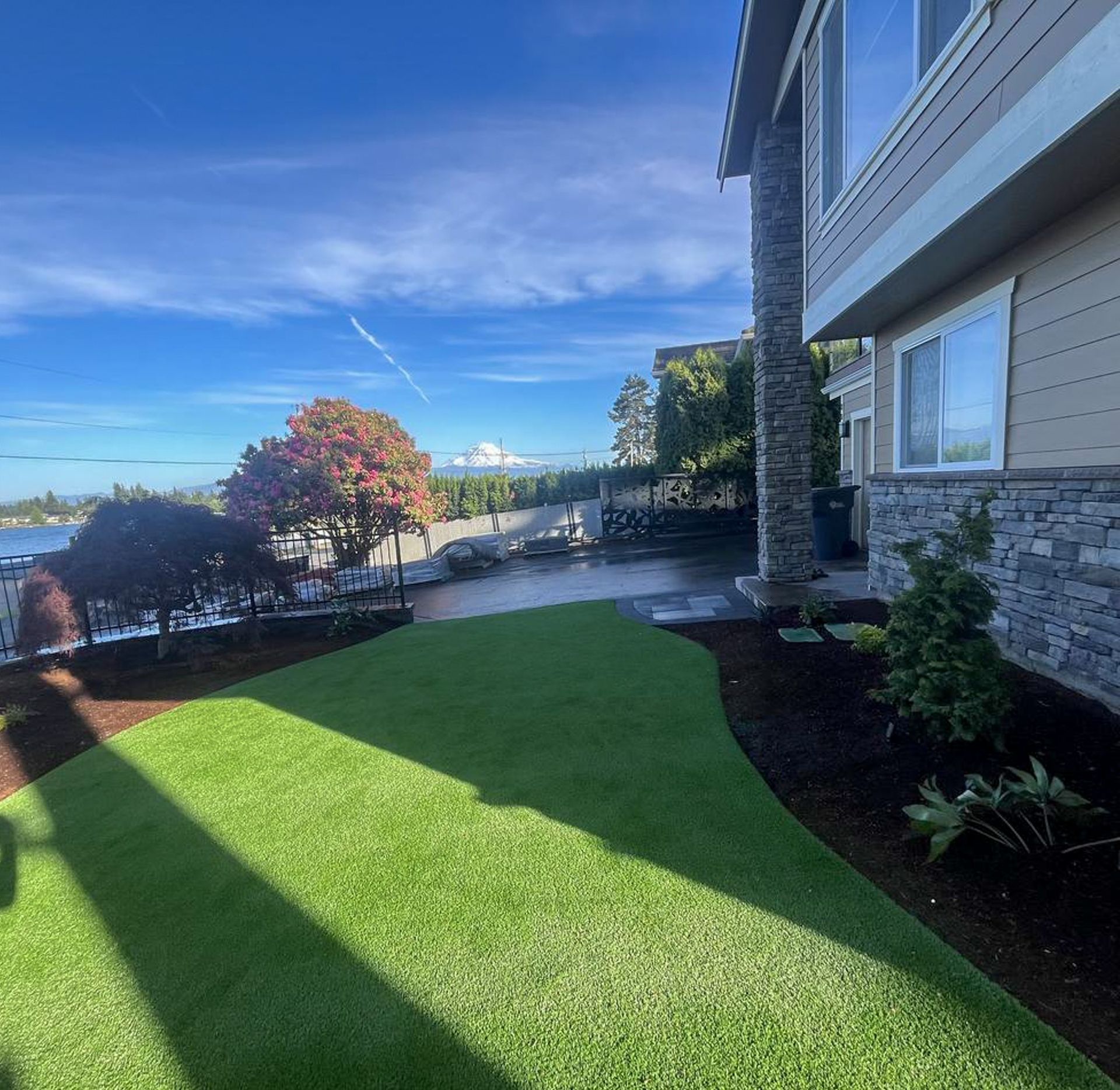 Green lawn in front of house with lake view, blue sky, trees, and stone accents.