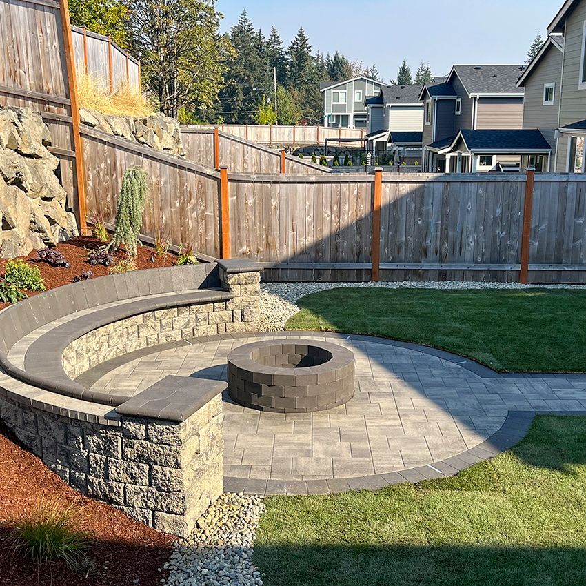 Backyard fire pit with curved stone seating, surrounded by grass and pavers.