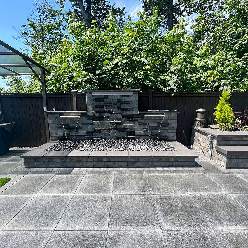 Backyard water feature with waterfall, fireplace, and patio pavers.