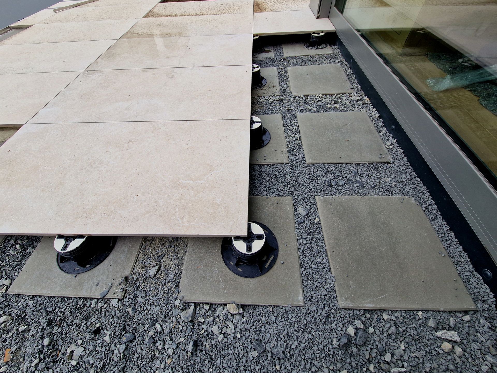 Raised patio tiles supported by adjustable pedestals on gravel.