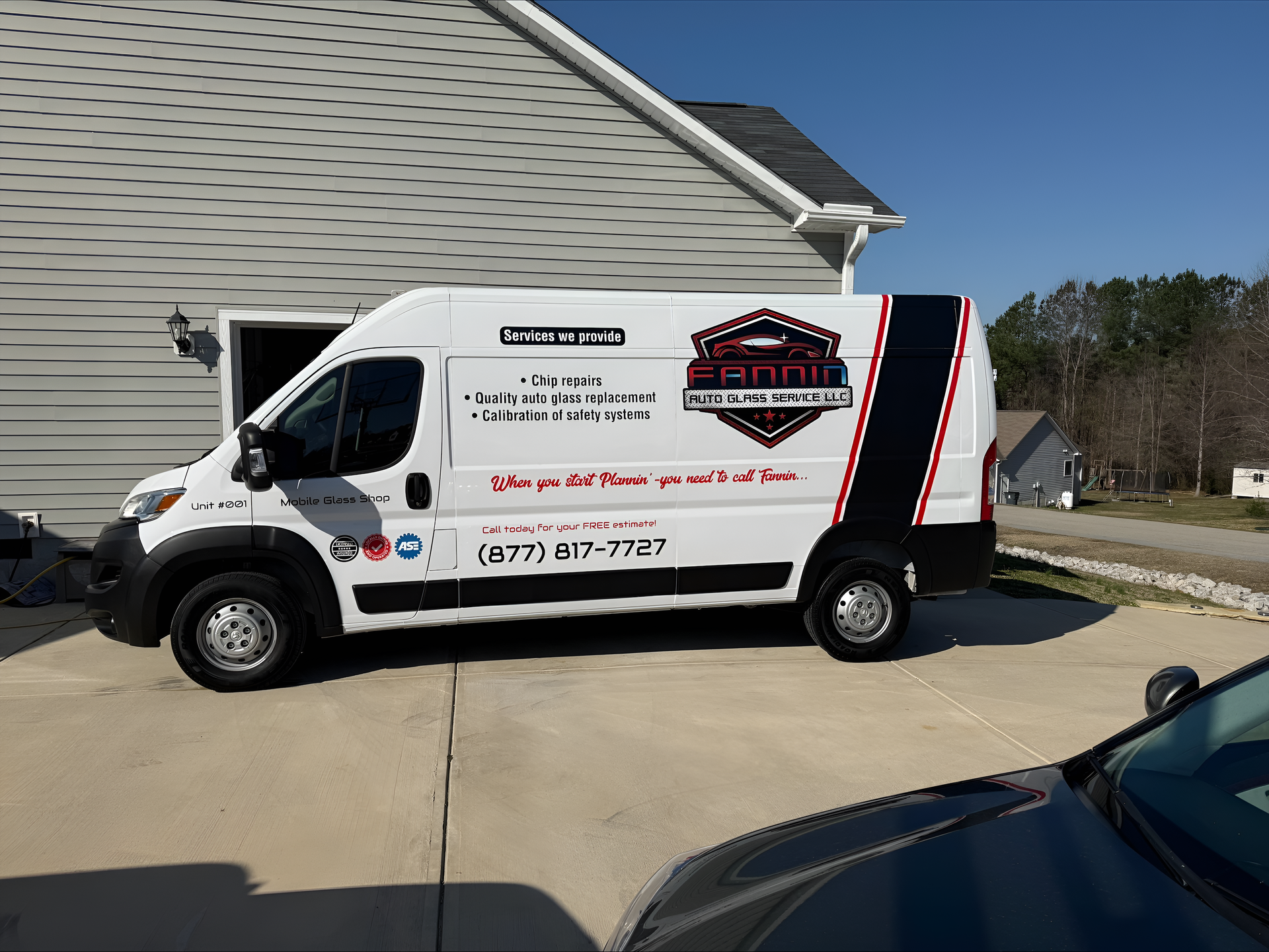 White service van with business decals parked beside a house driveway on a sunny day