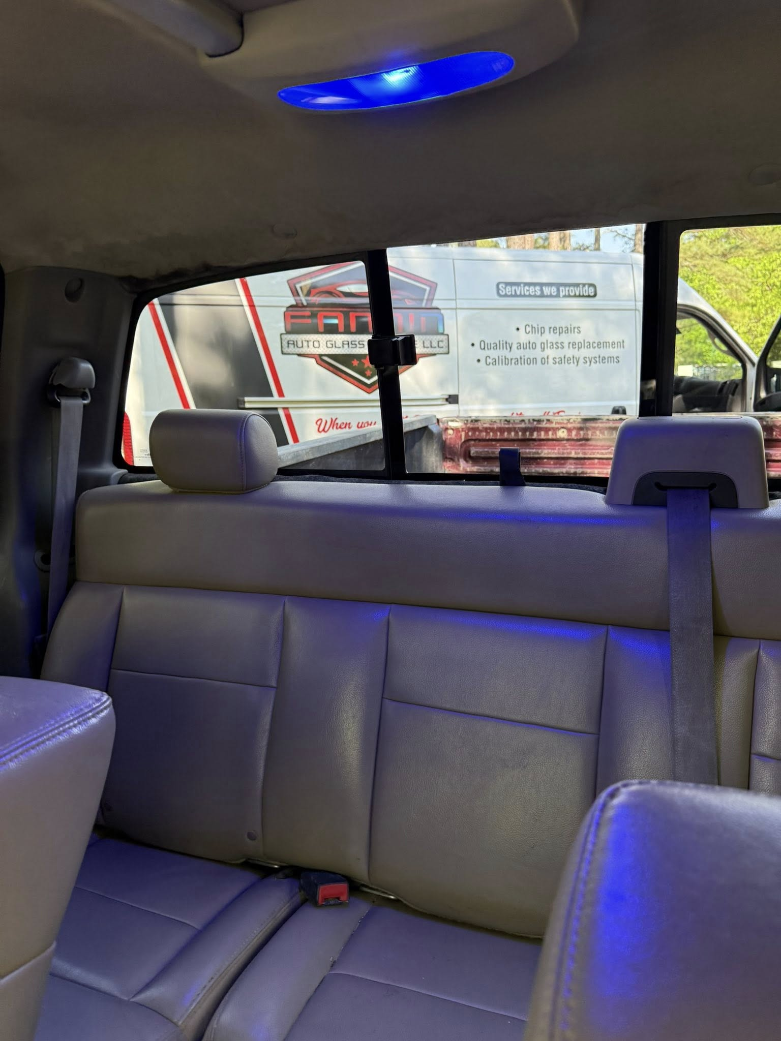 Interior of a vehicle with gray seats and blue ceiling light, looking out the rear window at traffic behind