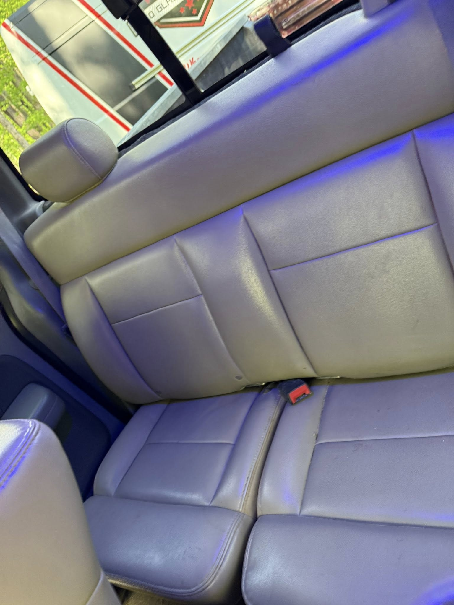 Gray leather back seat in a car with a blue-purple interior light and a seat belt buckle visible