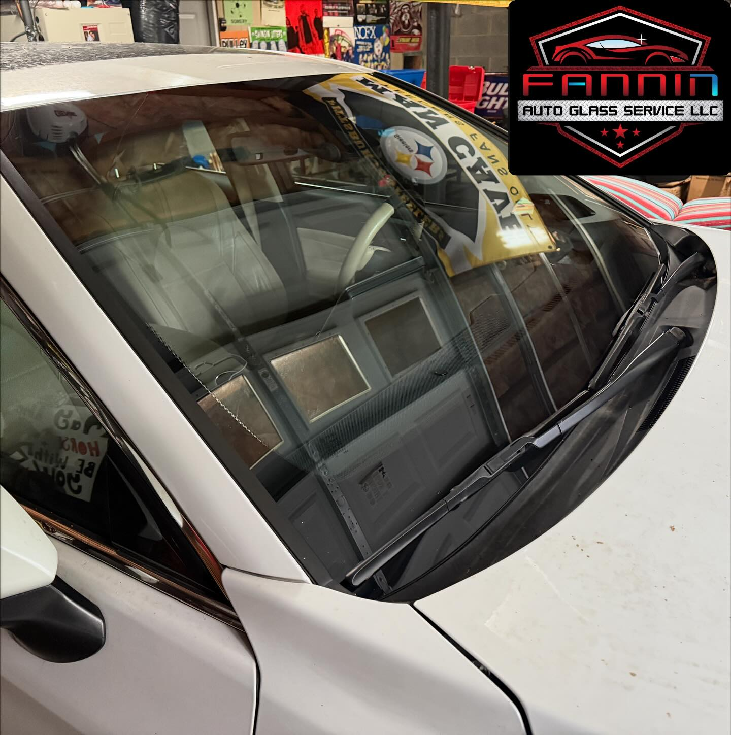 White car windshield in an auto detailing shop, with a logo reflected in the glass.