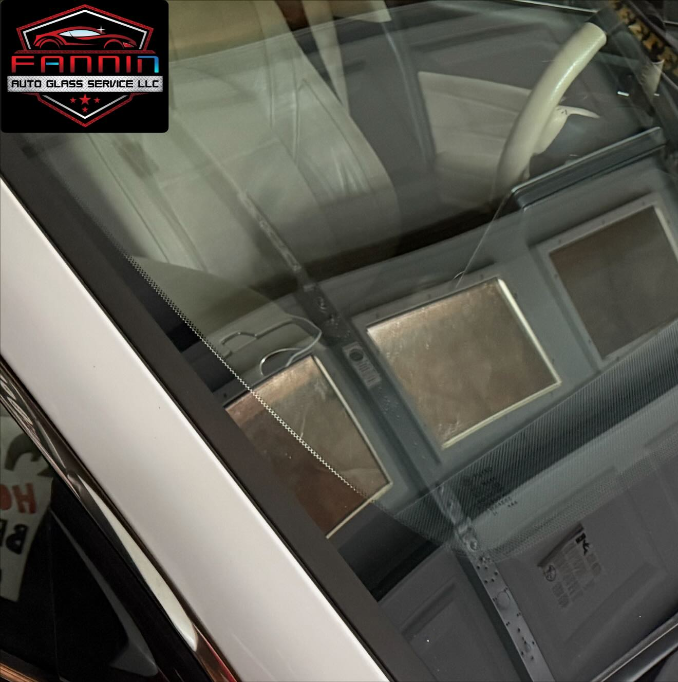Close-up of a car windshield and dashboard with a small logo sticker in the corner