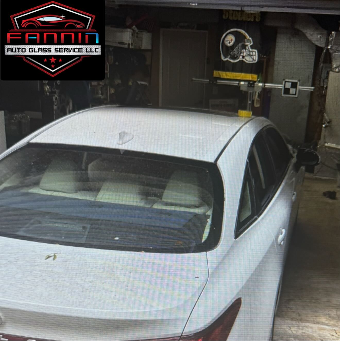 White sedan parked outside an auto glass service shop under a covered bay.