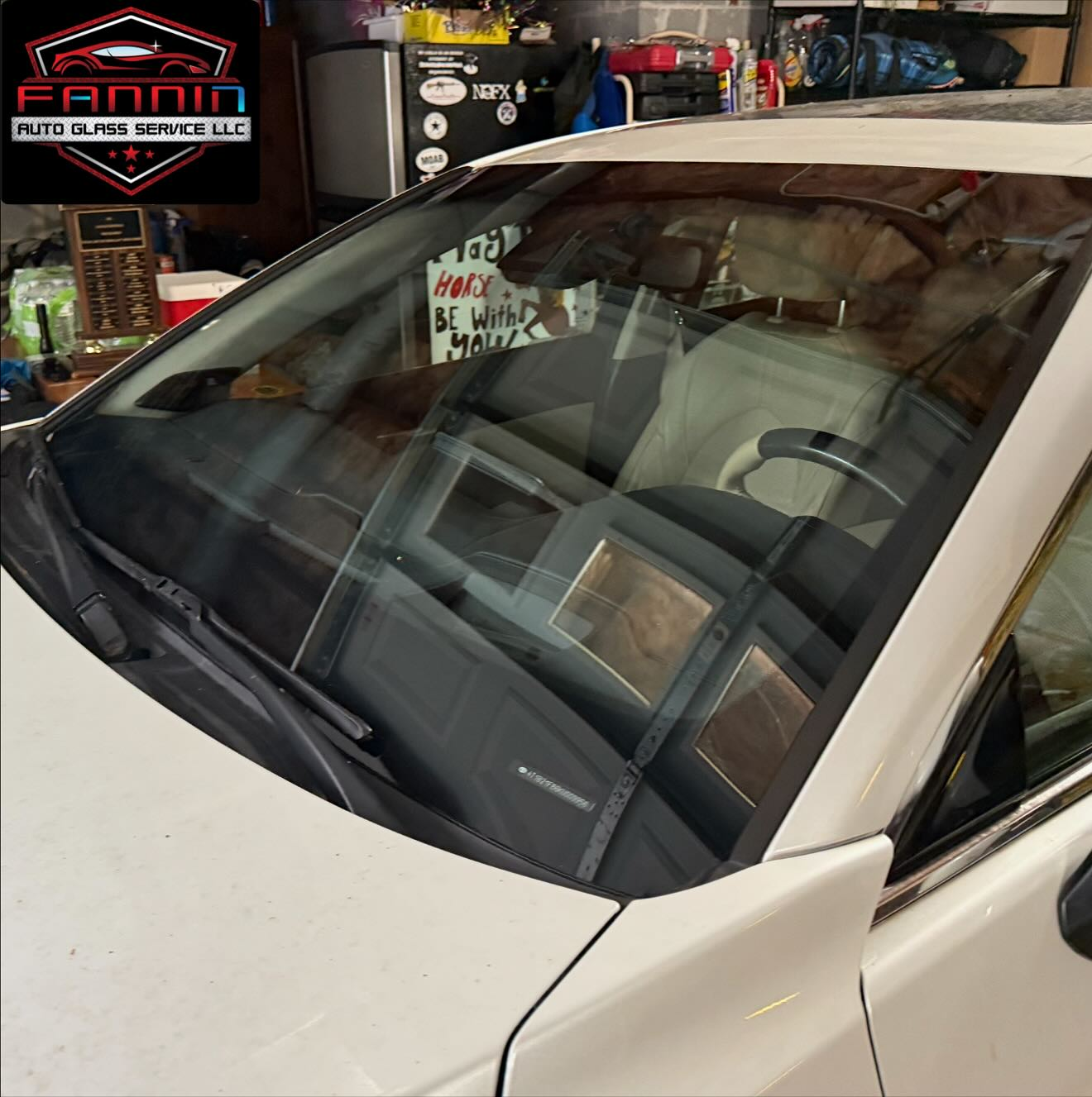 White car windshield in a garage, with reflections of shelves and tools inside the workshop.