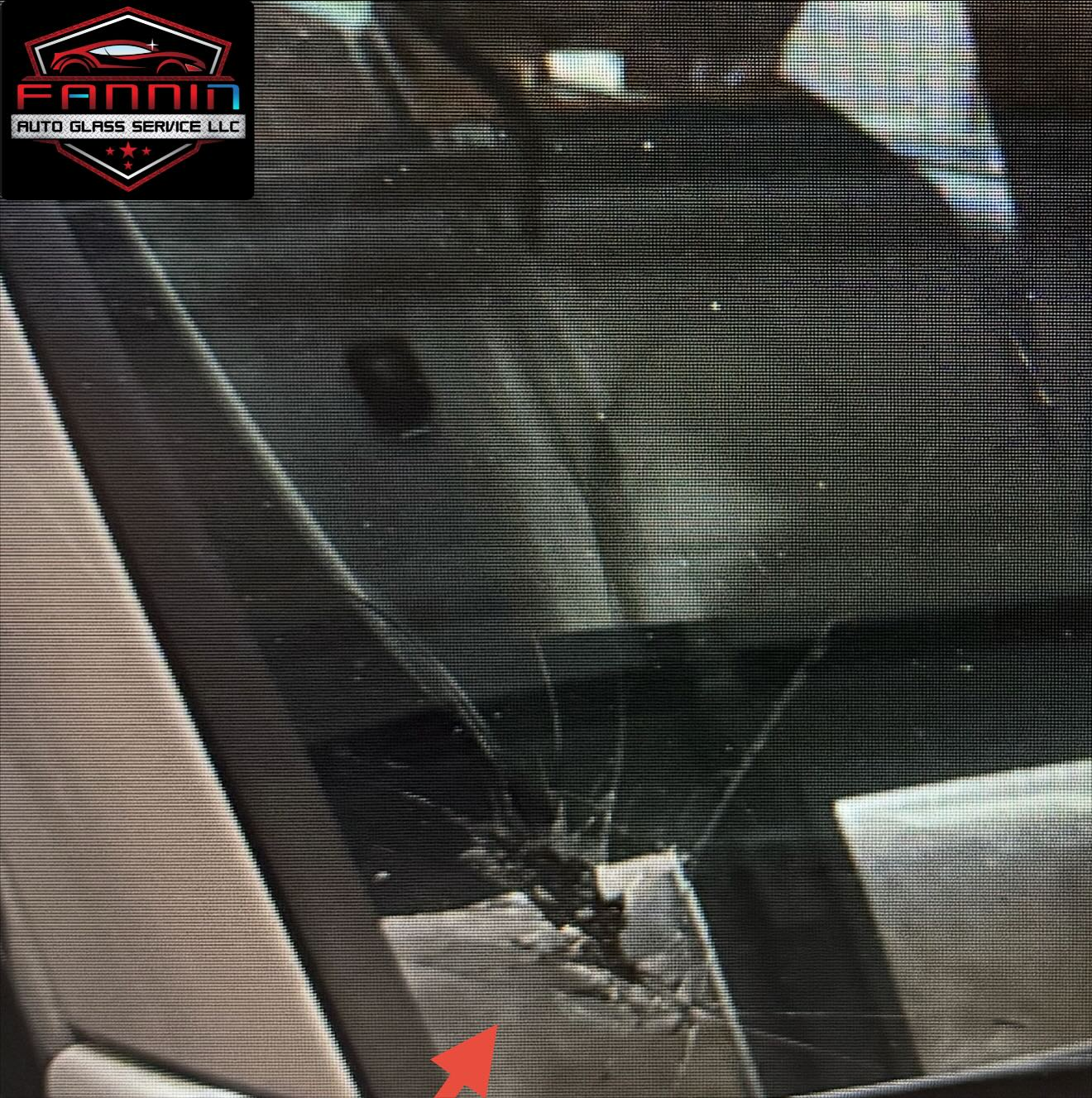 Cracked windshield with a large spiderweb fracture near the lower center, marked by a red arrow.
