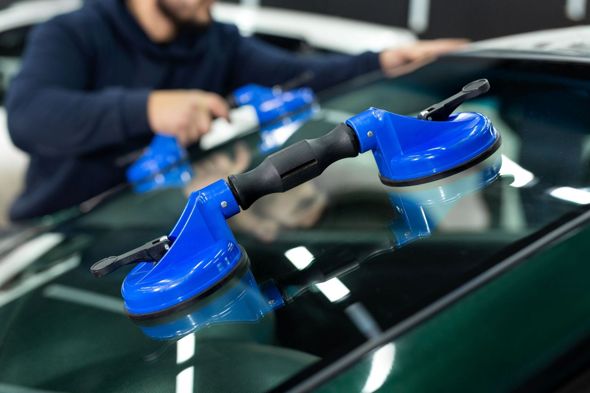 Blue suction cup tool attached to a car windshield, with a blurred person in the background