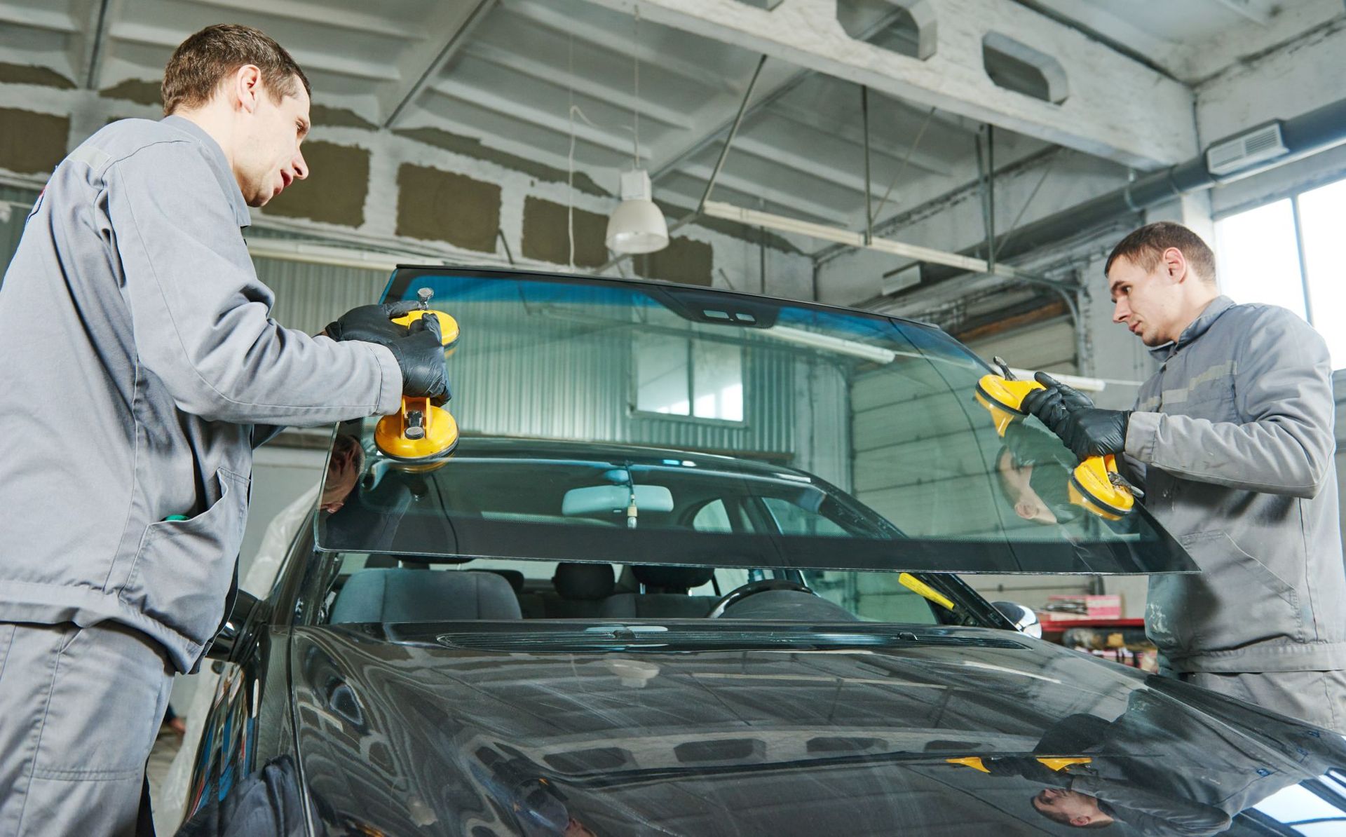 Two technicians polishing a black car windshield in an auto repair shop