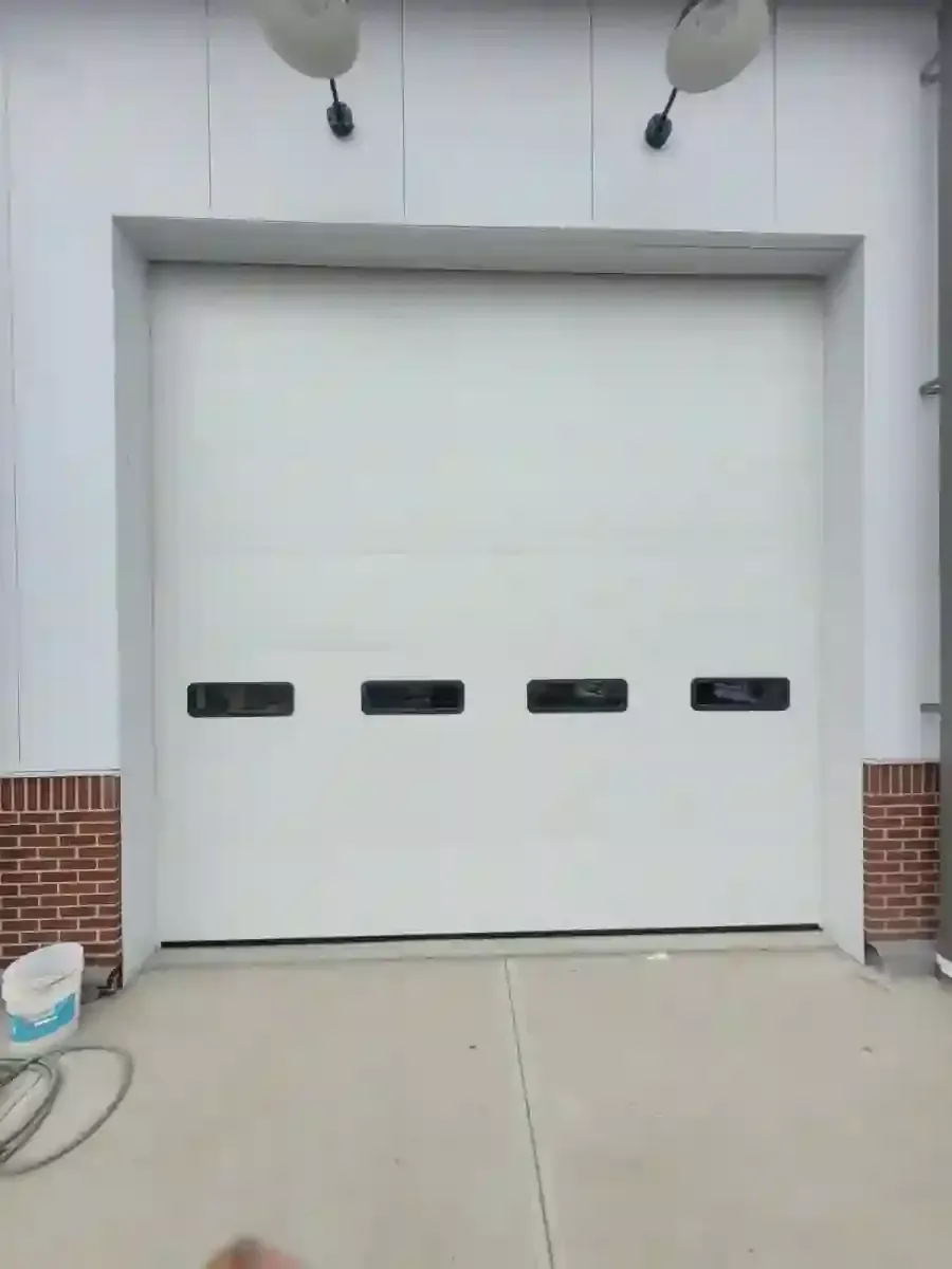 Closed white garage door in a building facade with brick sides and small rectangular windows.