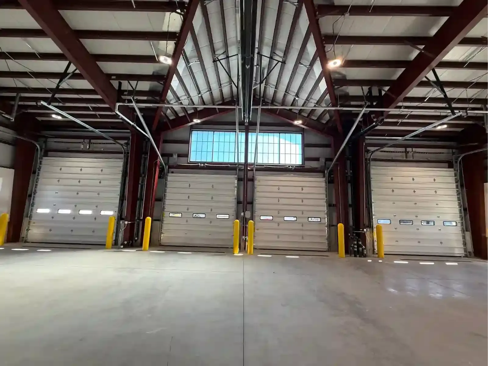 Empty warehouse loading dock with four closed bay doors and high metal ceiling